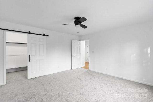 unfurnished bedroom with a walk in closet, ceiling fan, a closet, and light colored carpet