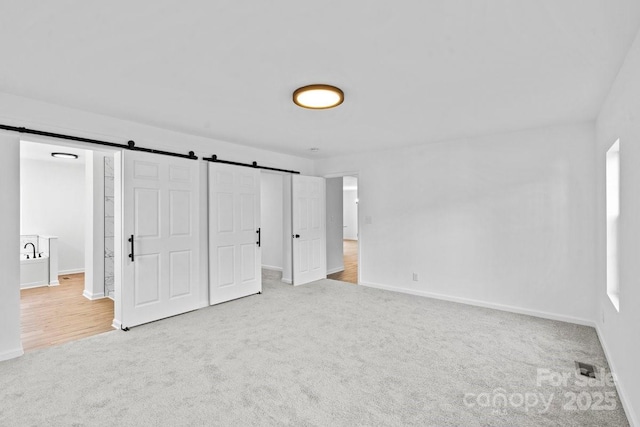 unfurnished bedroom featuring a barn door and light colored carpet