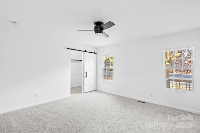 carpeted spare room with a barn door and ceiling fan