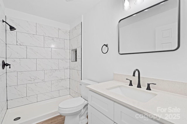 bathroom featuring hardwood / wood-style floors, vanity, toilet, and tiled shower