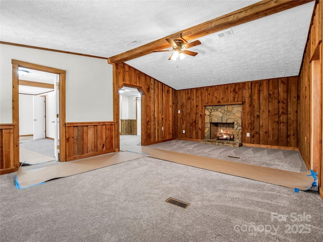 unfurnished living room featuring ceiling fan, vaulted ceiling with beams, a stone fireplace, a textured ceiling, and ornamental molding