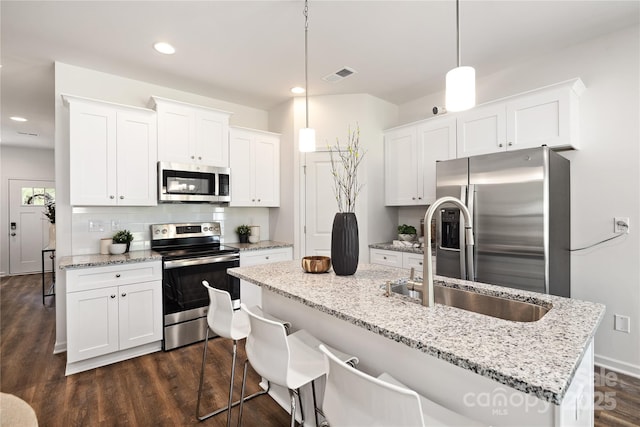 kitchen with appliances with stainless steel finishes, dark hardwood / wood-style flooring, white cabinetry, hanging light fixtures, and an island with sink