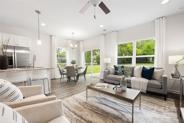 living room featuring plenty of natural light, sink, light hardwood / wood-style floors, and ceiling fan with notable chandelier