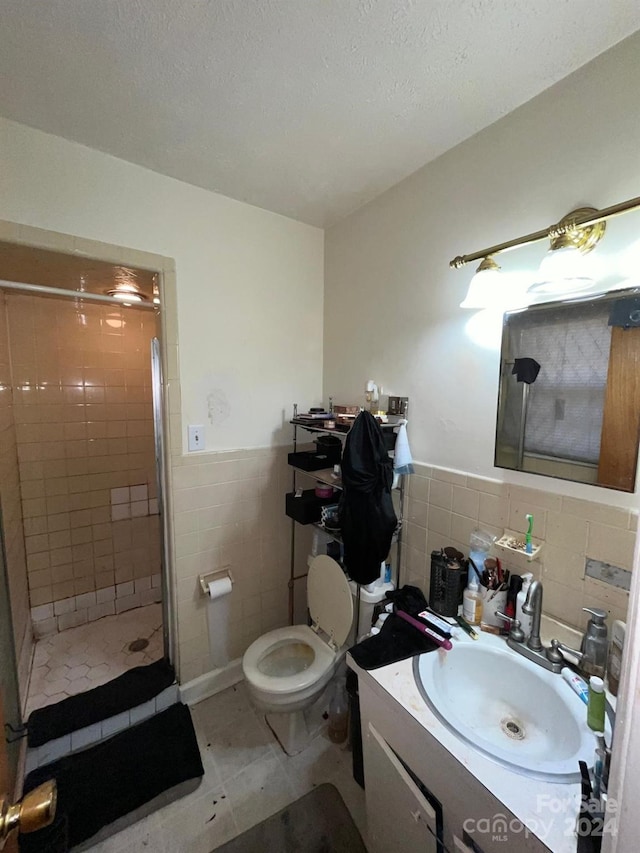 bathroom featuring tile patterned floors, a tile shower, vanity, tile walls, and toilet