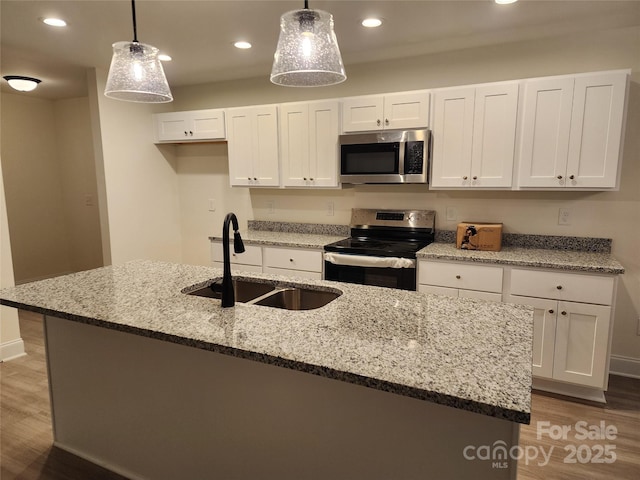 kitchen with pendant lighting, appliances with stainless steel finishes, sink, white cabinets, and an island with sink