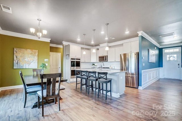 kitchen with decorative light fixtures, white cabinetry, an island with sink, and appliances with stainless steel finishes