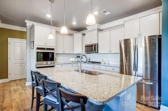 kitchen featuring sink, hanging light fixtures, stainless steel appliances, a breakfast bar area, and a center island with sink