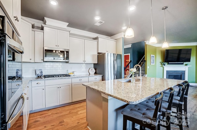 kitchen with pendant lighting, a center island with sink, a kitchen breakfast bar, sink, and appliances with stainless steel finishes