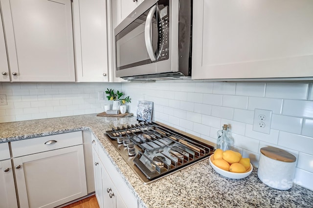 kitchen featuring tasteful backsplash, light stone counters, white cabinets, and stainless steel appliances