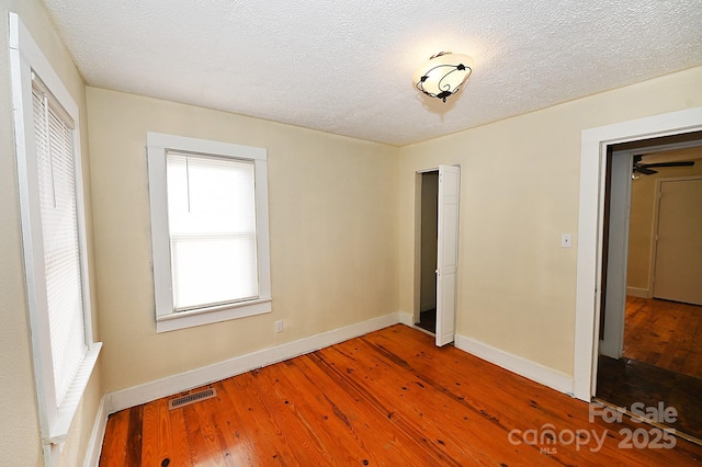 unfurnished bedroom featuring multiple windows, hardwood / wood-style floors, and a textured ceiling