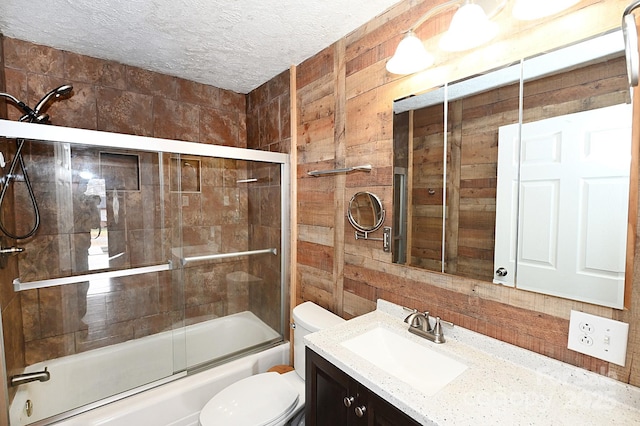 full bathroom with wood walls, bath / shower combo with glass door, a textured ceiling, toilet, and vanity