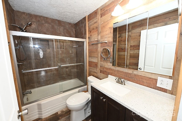 full bathroom featuring vanity, a textured ceiling, enclosed tub / shower combo, toilet, and wood walls