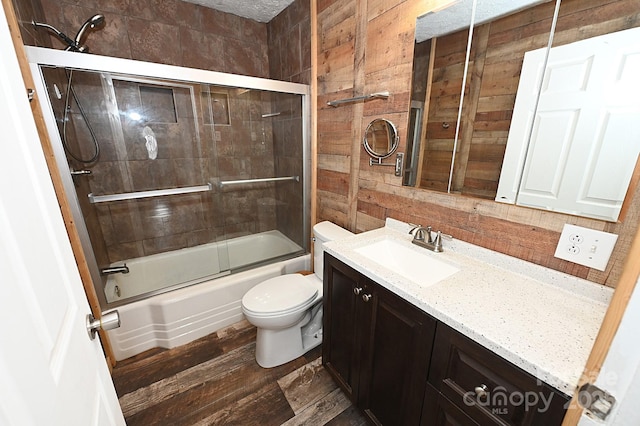 full bathroom featuring hardwood / wood-style floors, vanity, combined bath / shower with glass door, wooden walls, and toilet