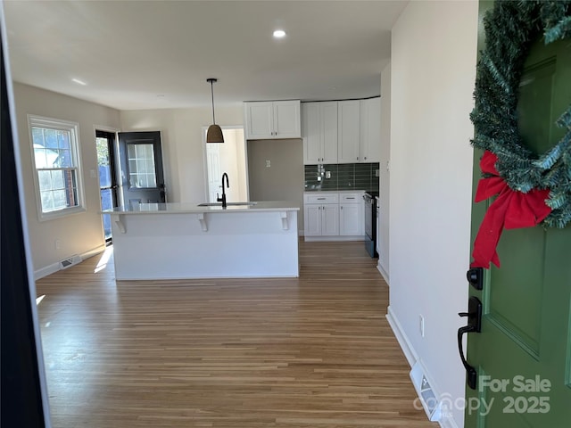 kitchen with tasteful backsplash, a kitchen island with sink, sink, decorative light fixtures, and white cabinets