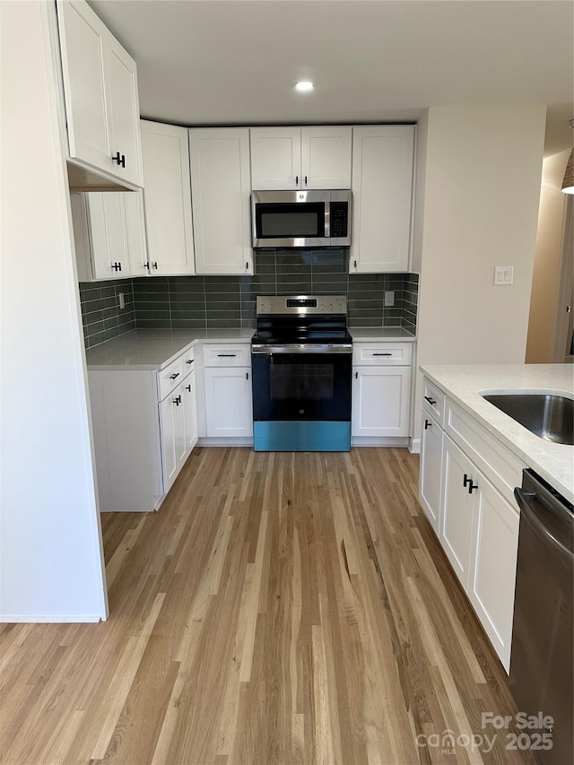 kitchen with tasteful backsplash, white cabinetry, light wood-type flooring, and appliances with stainless steel finishes