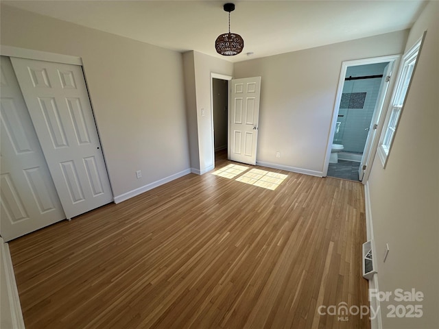 unfurnished bedroom with wood-type flooring, connected bathroom, and a closet