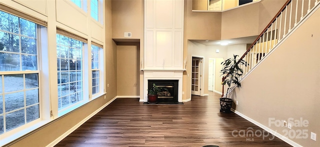 unfurnished living room featuring a large fireplace, a towering ceiling, and dark wood-type flooring