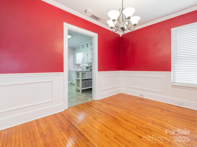 spare room featuring a notable chandelier, wood-type flooring, and crown molding