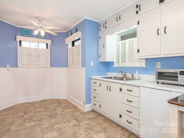 kitchen with ceiling fan, sink, white cabinets, and ornamental molding