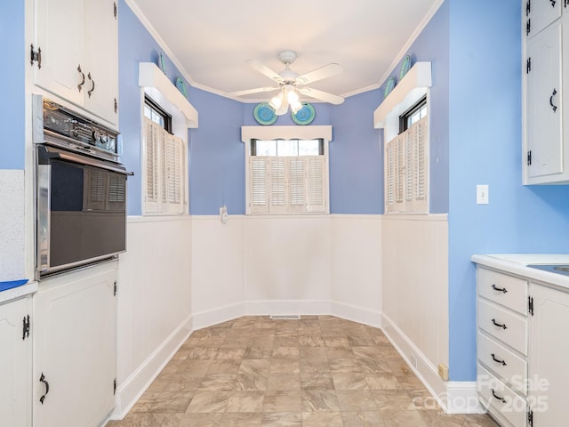 kitchen with black oven, ceiling fan, white cabinetry, and ornamental molding