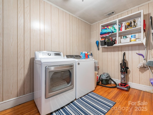 clothes washing area with washer and clothes dryer, wood walls, crown molding, and hardwood / wood-style flooring