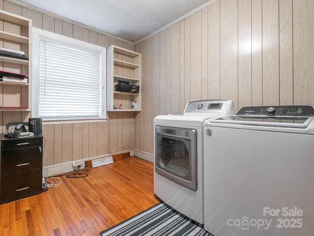 laundry area with washing machine and dryer, light hardwood / wood-style floors, crown molding, and wooden walls