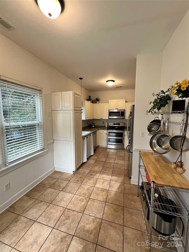 kitchen featuring pendant lighting, light tile patterned floors, stainless steel appliances, and white cabinetry