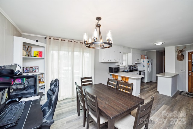 dining room with sink, light hardwood / wood-style flooring, ornamental molding, and a chandelier