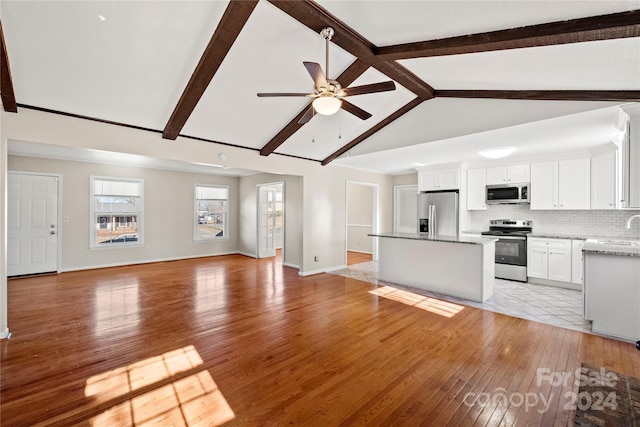 kitchen featuring appliances with stainless steel finishes, tasteful backsplash, a center island, vaulted ceiling with beams, and white cabinetry