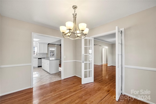 unfurnished dining area with french doors, light hardwood / wood-style floors, and an inviting chandelier