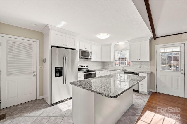 kitchen with beamed ceiling, appliances with stainless steel finishes, white cabinetry, and sink