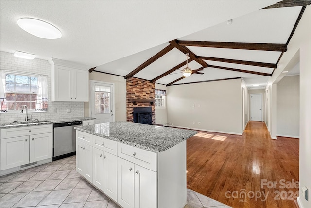 kitchen featuring dishwasher, a center island, lofted ceiling with beams, sink, and white cabinetry