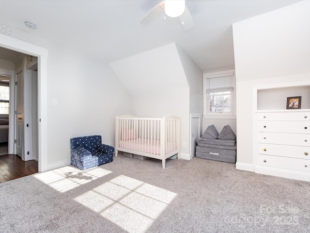 carpeted bedroom with a crib, vaulted ceiling, and ceiling fan