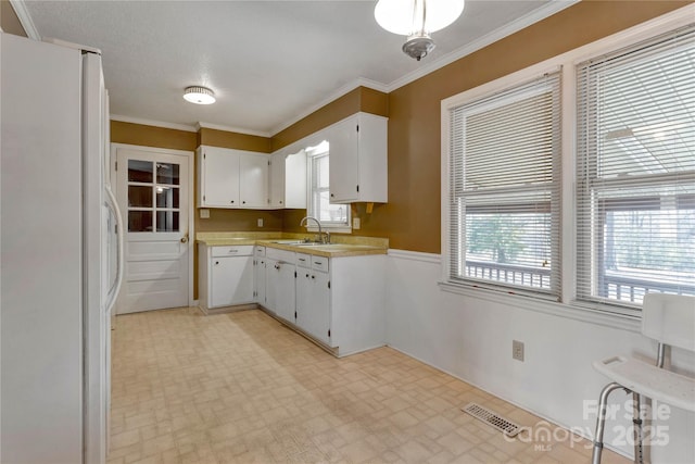 kitchen with white cabinets, white refrigerator, ornamental molding, and sink