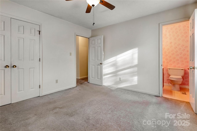 unfurnished bedroom with ceiling fan, a closet, light carpet, and ensuite bath