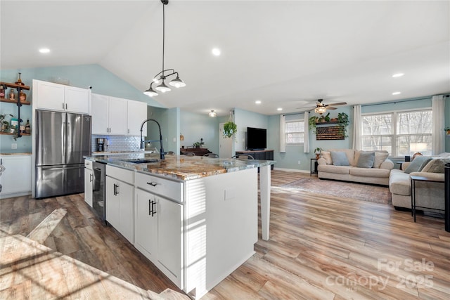 kitchen with stainless steel refrigerator, light stone countertops, hanging light fixtures, an island with sink, and white cabinets