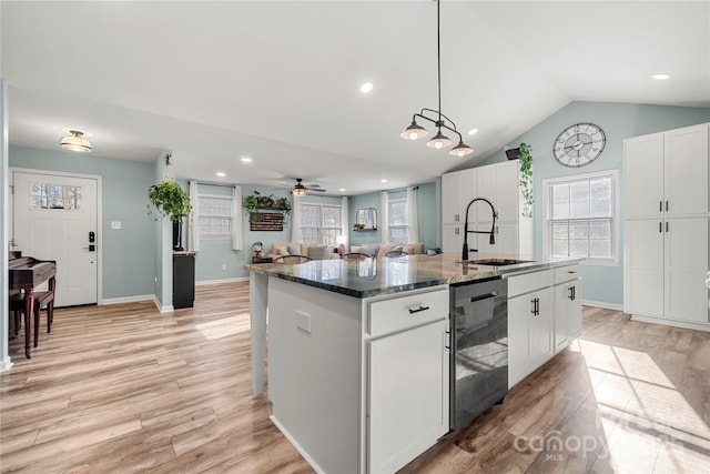 kitchen with ceiling fan, sink, dark stone countertops, white cabinets, and an island with sink