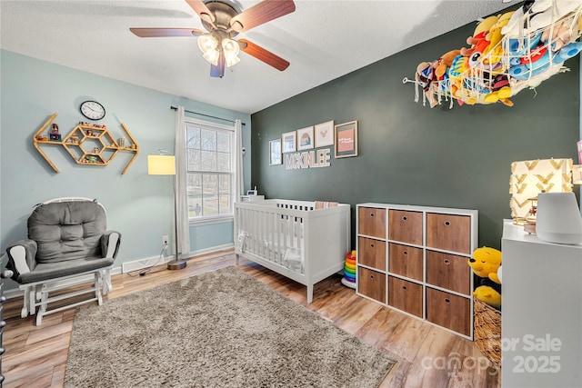 bedroom with a textured ceiling, light hardwood / wood-style floors, a nursery area, and ceiling fan