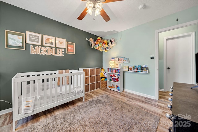 bedroom with ceiling fan, a nursery area, a textured ceiling, and wood-type flooring