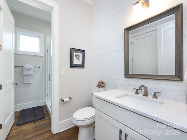 full bath featuring toilet, a stall shower, vanity, wood finished floors, and baseboards