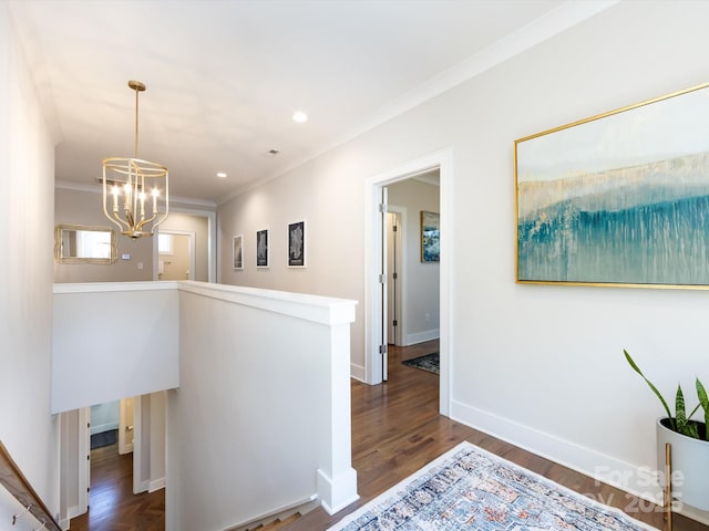 hall with dark wood finished floors, ornamental molding, an upstairs landing, a chandelier, and baseboards