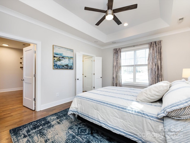 bedroom with a tray ceiling, visible vents, a ceiling fan, wood finished floors, and baseboards