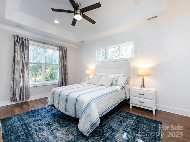 bedroom featuring a tray ceiling, visible vents, baseboards, and wood finished floors