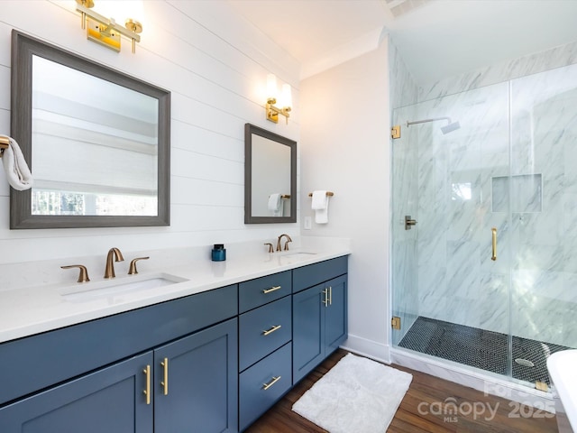 full bathroom with double vanity, wood finished floors, a sink, and a marble finish shower