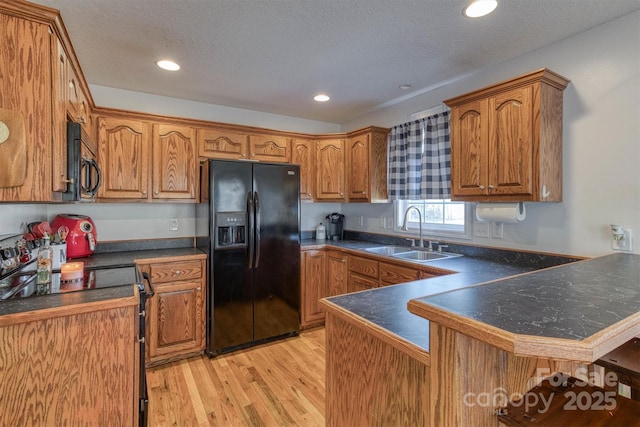 kitchen featuring black appliances, sink, light hardwood / wood-style flooring, a textured ceiling, and kitchen peninsula