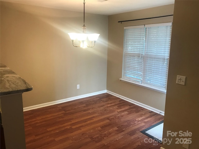 unfurnished dining area featuring dark wood-type flooring and an inviting chandelier