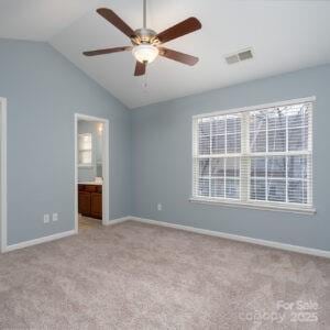 unfurnished bedroom with light carpet, ensuite bathroom, vaulted ceiling, and multiple windows