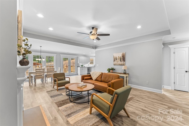 living room with ceiling fan with notable chandelier, light hardwood / wood-style flooring, and ornamental molding