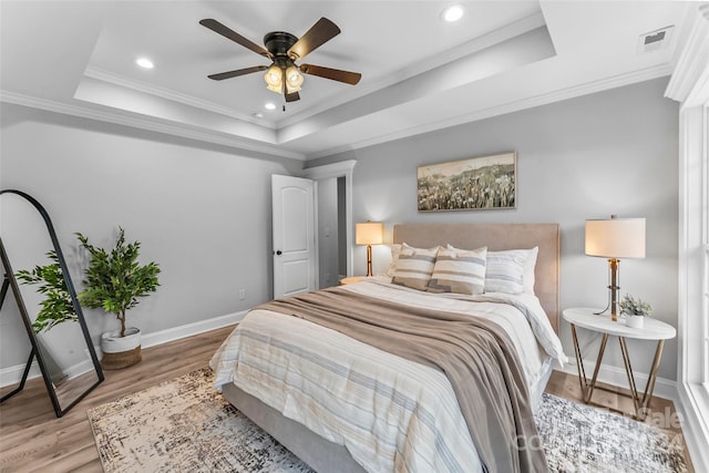 bedroom with wood-type flooring, a tray ceiling, ceiling fan, and ornamental molding