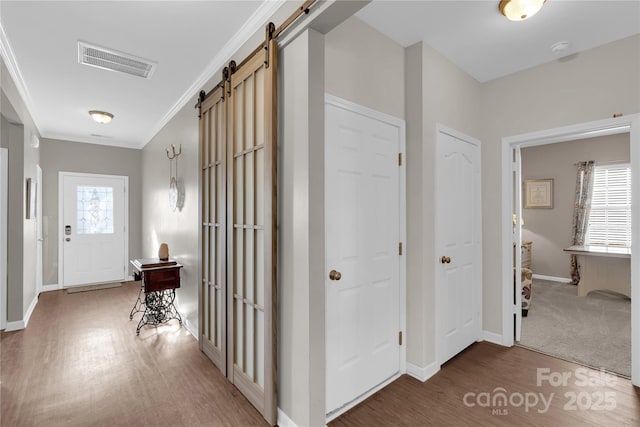 hall with carpet flooring, a barn door, plenty of natural light, and ornamental molding